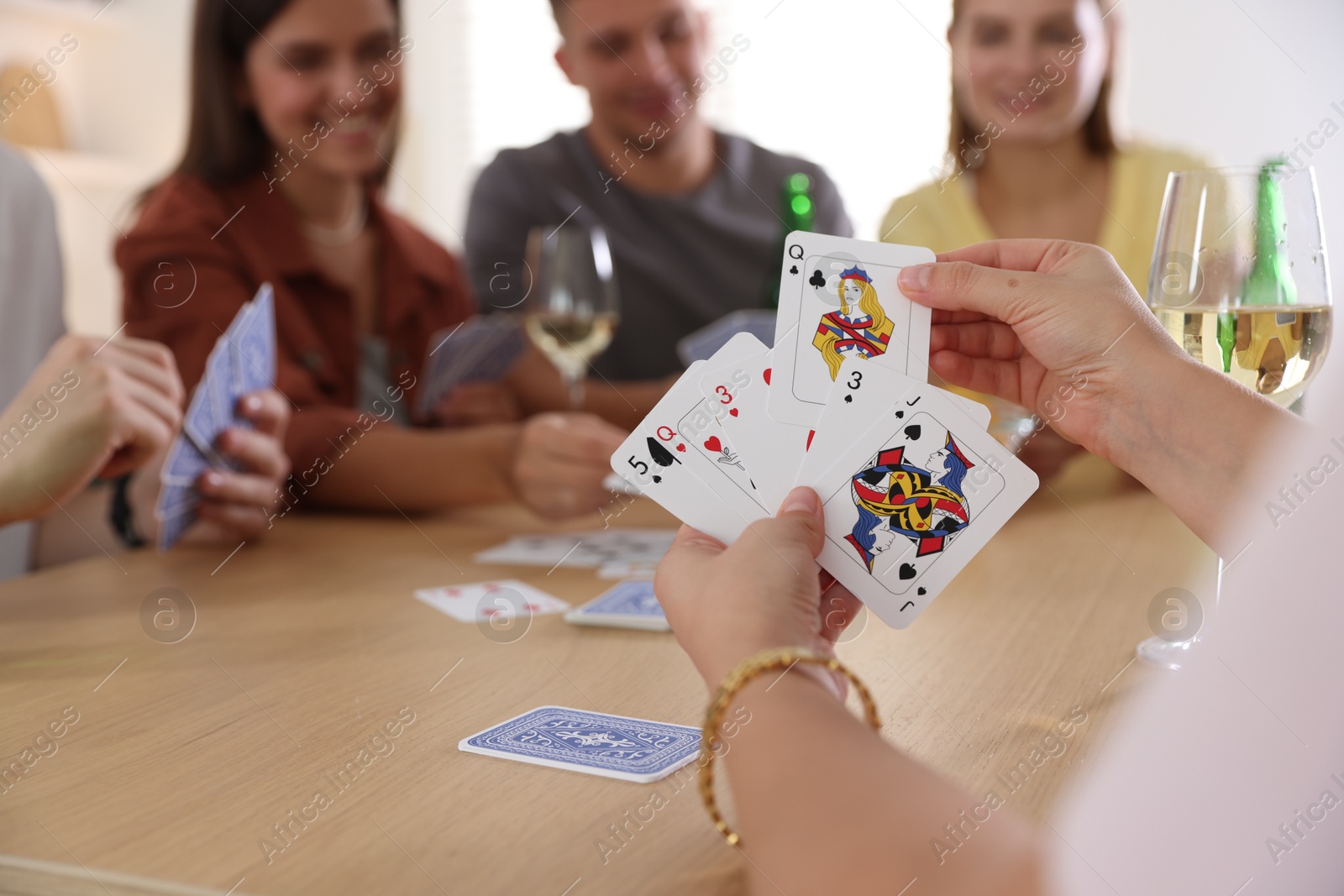 Photo of Group of friends playing cards at wooden table indoors, selective focus