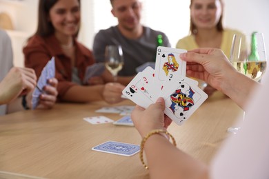 Photo of Group of friends playing cards at wooden table indoors, selective focus