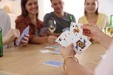 Photo of Group of friends playing cards at wooden table indoors, selective focus