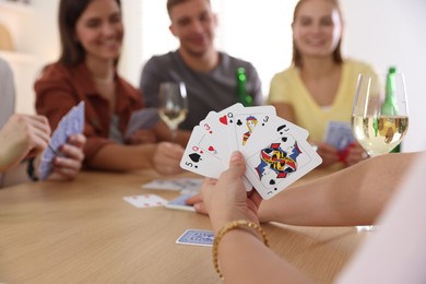 Photo of Group of friends playing cards at wooden table indoors, selective focus