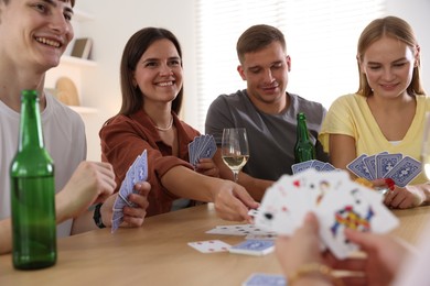 Photo of Group of friends playing cards at wooden table indoors