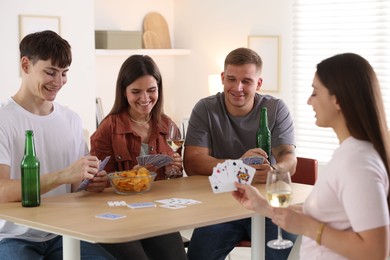 Photo of Group of friends playing cards at wooden table indoors