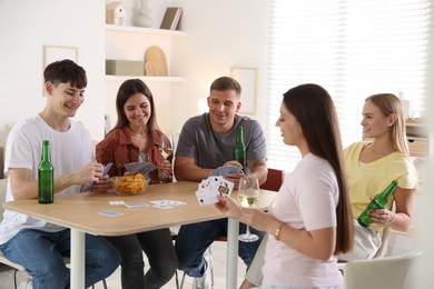 Photo of Group of friends playing cards at wooden table indoors