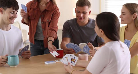 Photo of Group of friends playing cards at wooden table indoors