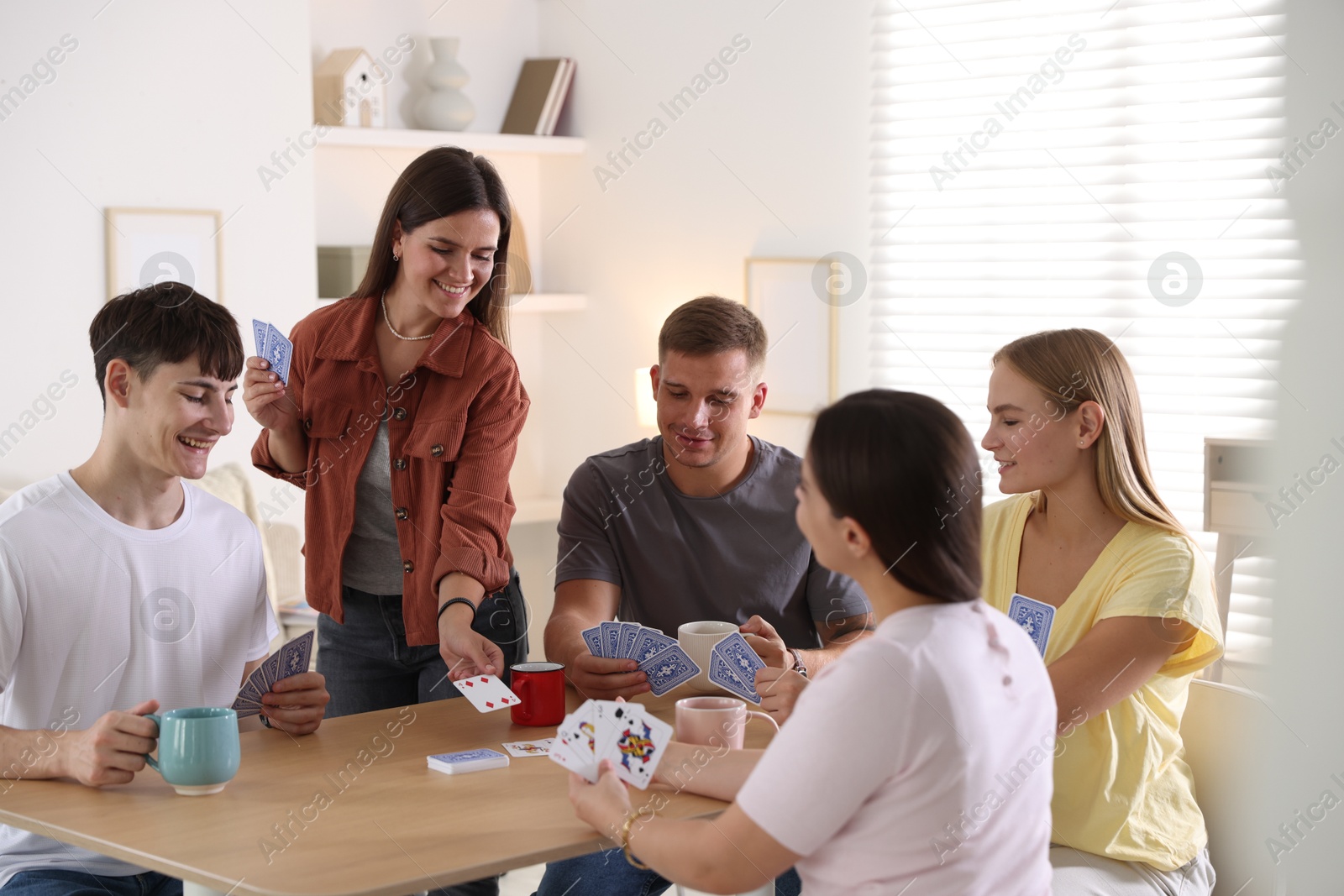 Photo of Group of friends playing cards at wooden table indoors