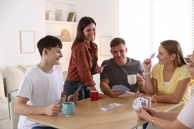 Photo of Group of friends playing cards at wooden table indoors