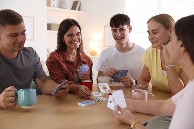 Photo of Group of friends playing cards at wooden table indoors