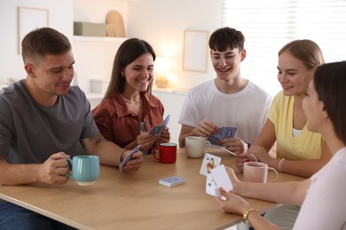 Photo of Group of friends playing cards at wooden table indoors