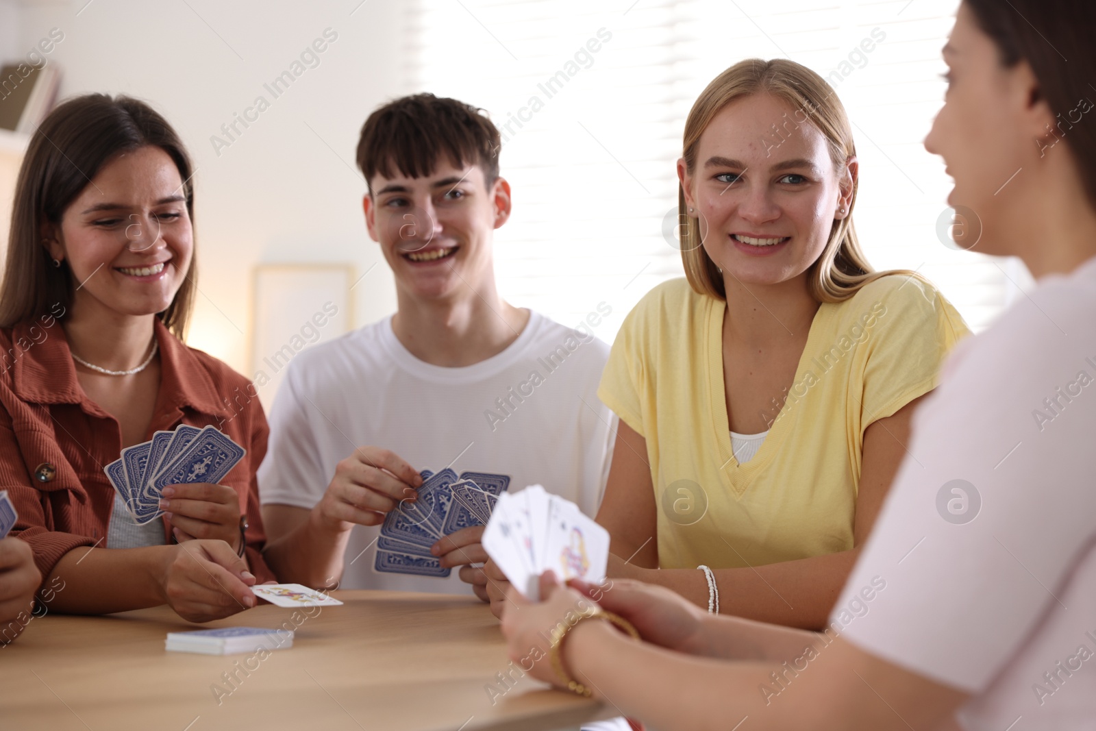 Photo of Group of friends playing cards at wooden table indoors