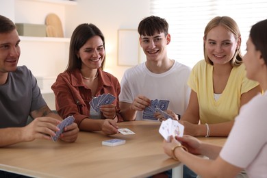 Photo of Group of friends playing cards at wooden table indoors