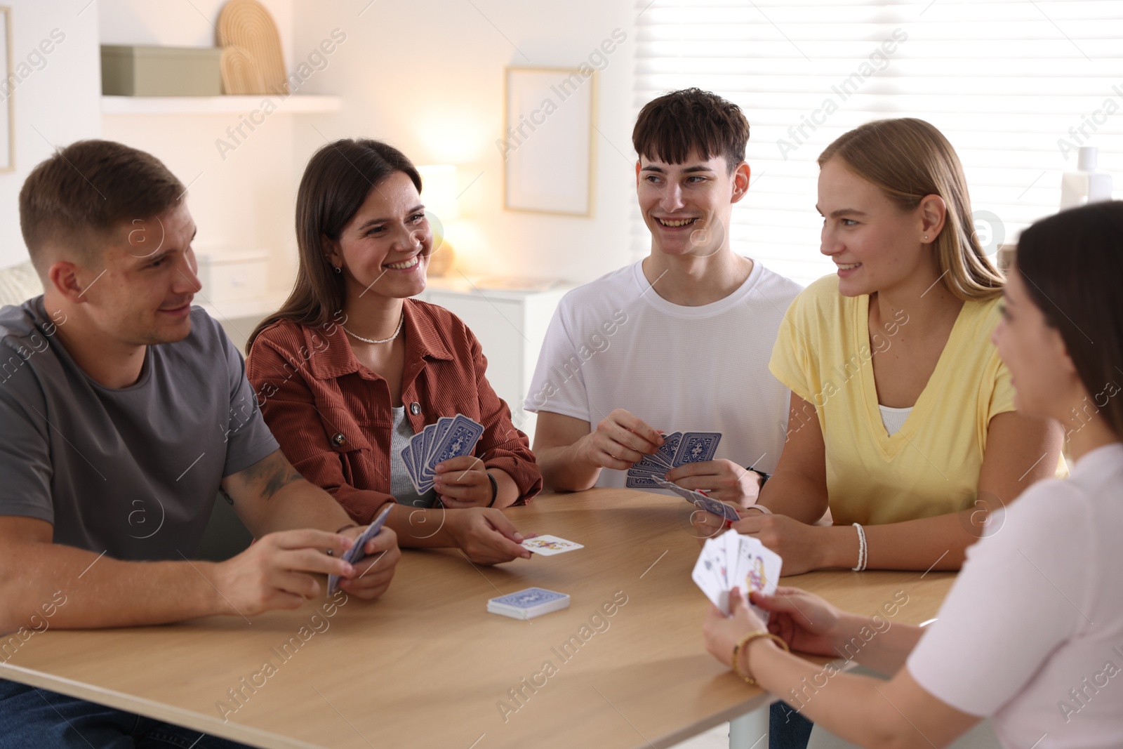 Photo of Group of friends playing cards at wooden table indoors