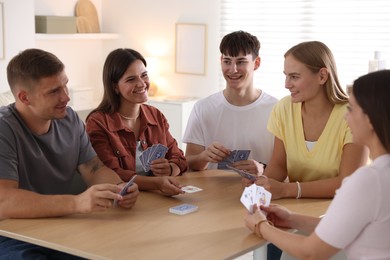 Photo of Group of friends playing cards at wooden table indoors