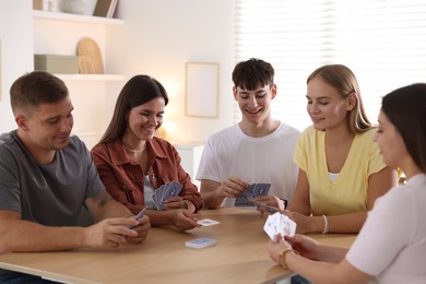 Photo of Group of friends playing cards at wooden table indoors