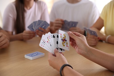 Photo of Group of friends playing cards at wooden table indoors, selective focus