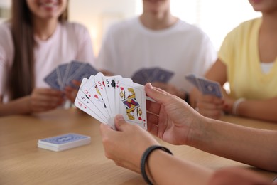 Photo of Group of friends playing cards at wooden table indoors, selective focus