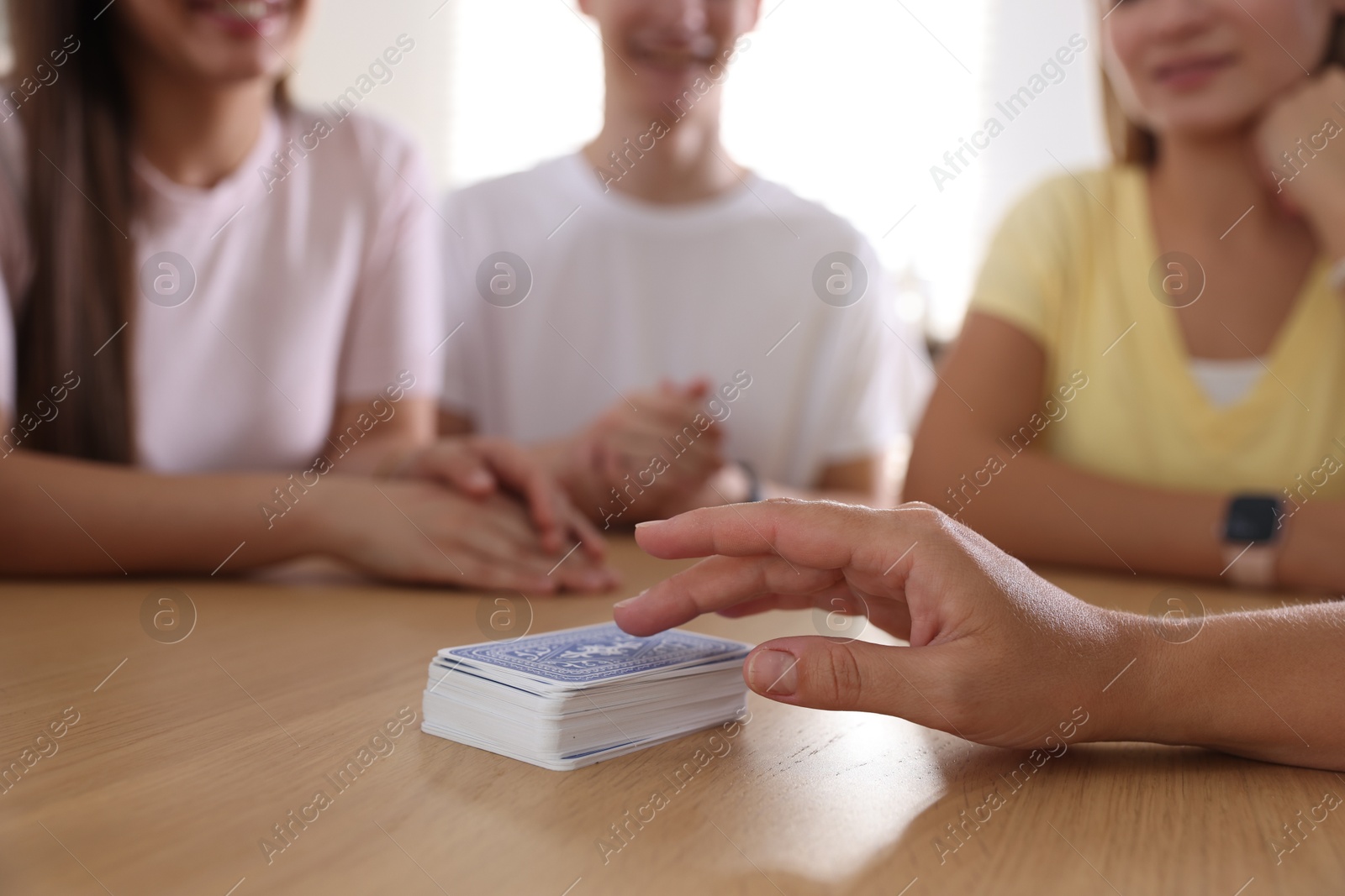 Photo of Group of friends playing cards at wooden table indoors, selective focus