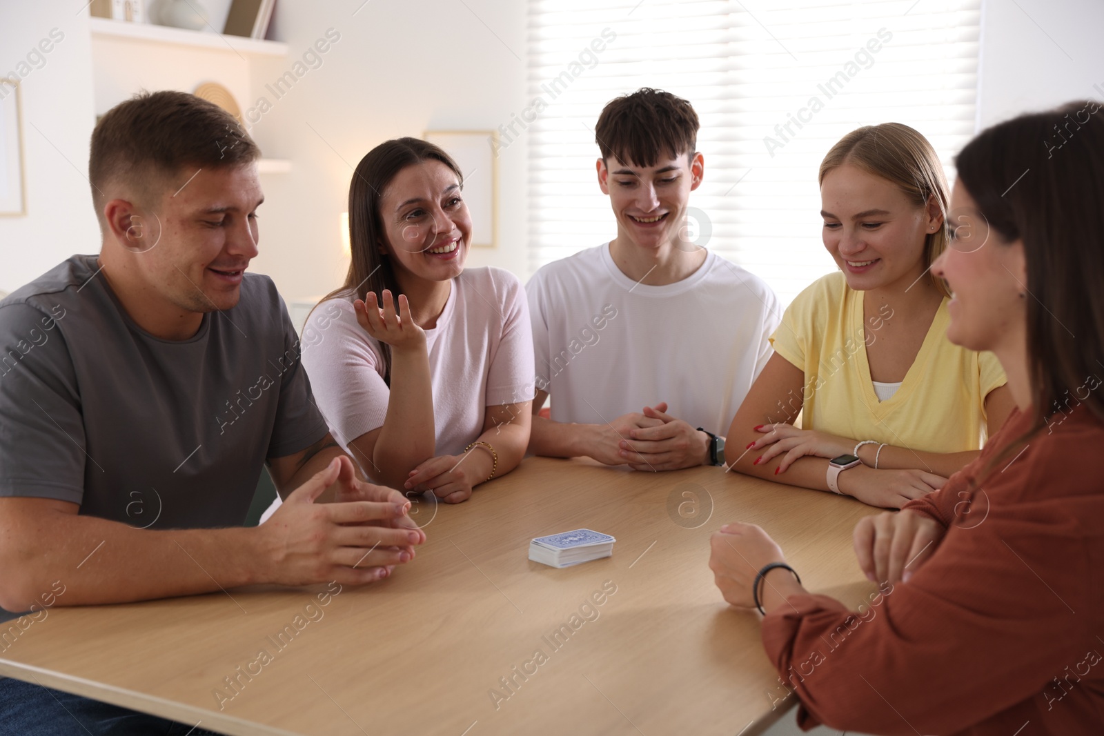Photo of Group of friends playing cards at wooden table indoors
