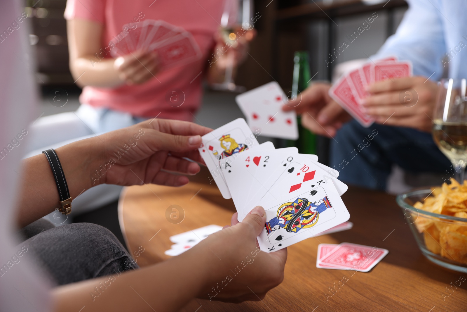 Photo of Friends playing cards at wooden table indoors, selective focus
