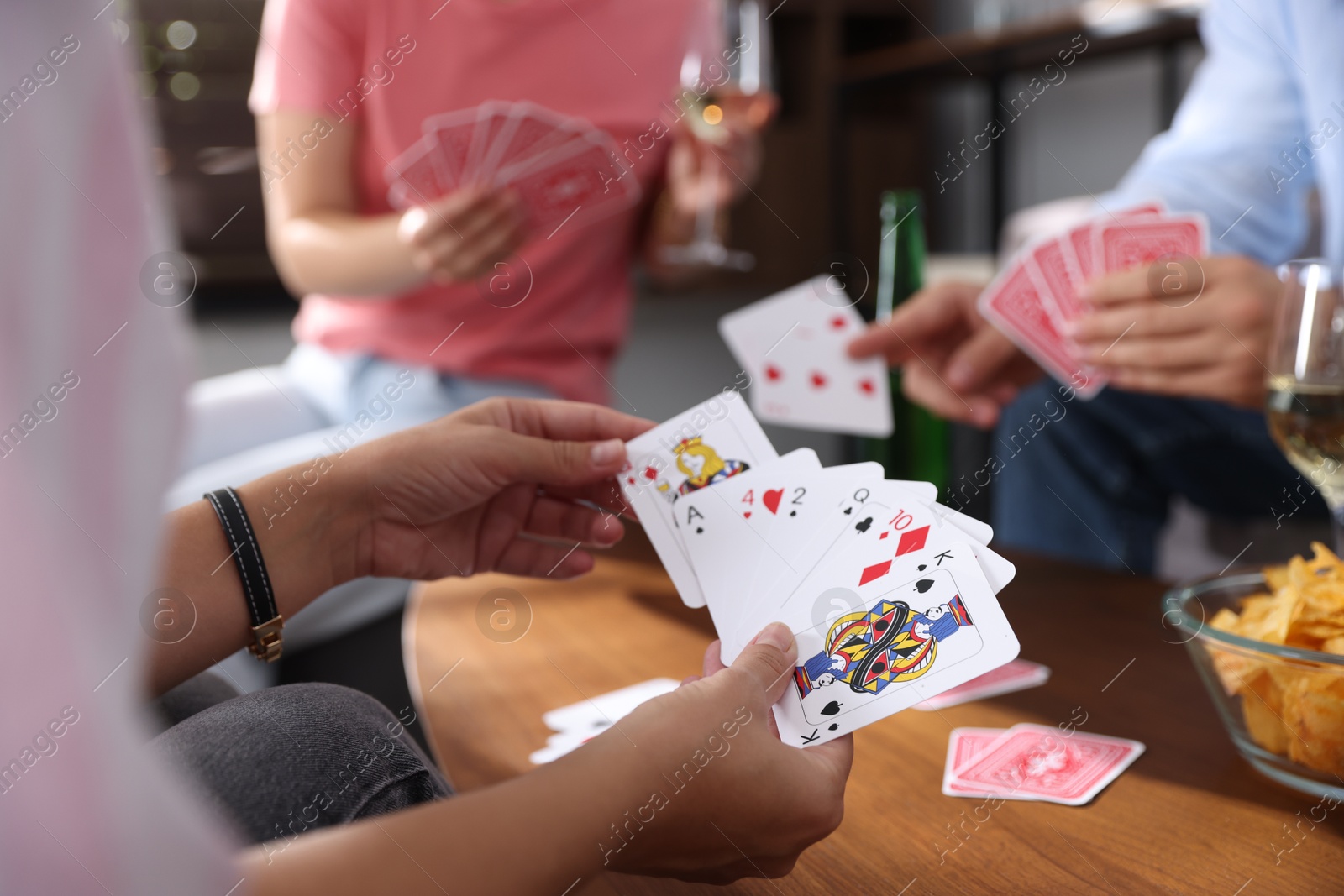 Photo of Friends playing cards at wooden table indoors, selective focus