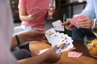 Photo of Friends playing cards at wooden table indoors, selective focus