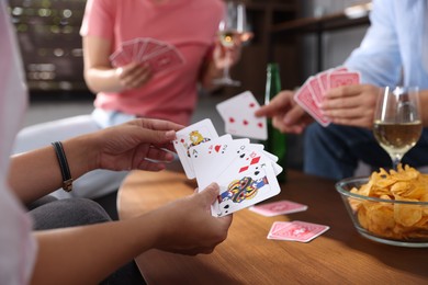 Photo of Friends playing cards at wooden table indoors, selective focus