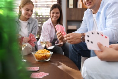 Photo of Group of friends playing cards at wooden table indoors, selective focus