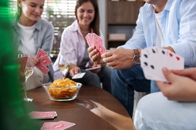 Photo of Group of friends playing cards at wooden table indoors, selective focus