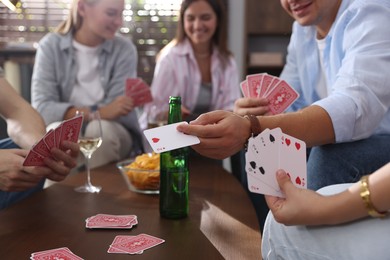 Photo of Group of friends playing cards at wooden table indoors, selective focus