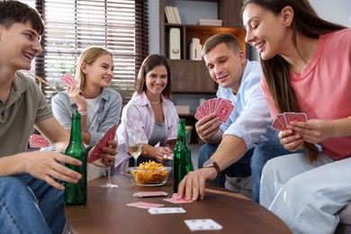 Photo of Group of friends playing cards at wooden table indoors