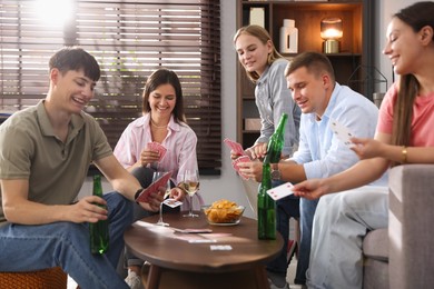 Photo of Group of friends playing cards at wooden table indoors