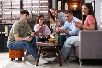Photo of Group of friends playing cards at wooden table indoors