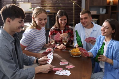 Photo of Group of friends playing cards at wooden table indoors