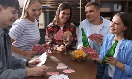 Photo of Group of friends playing cards at wooden table indoors
