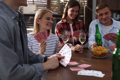Photo of Group of friends playing cards at wooden table indoors