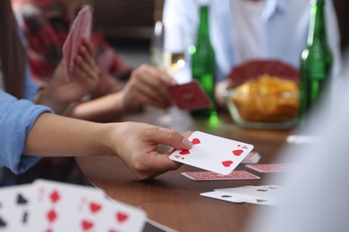 Photo of Friends playing cards at wooden table indoors, selective focus