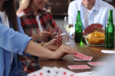 Photo of Friends playing cards at wooden table indoors, selective focus