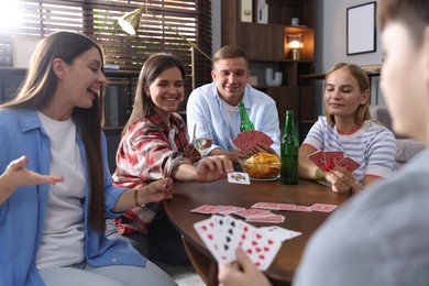 Photo of Group of friends playing cards at wooden table indoors