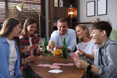 Photo of Group of friends playing cards at wooden table indoors