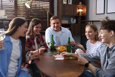 Photo of Group of friends playing cards at wooden table indoors