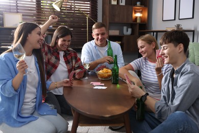 Photo of Group of friends playing cards at wooden table indoors