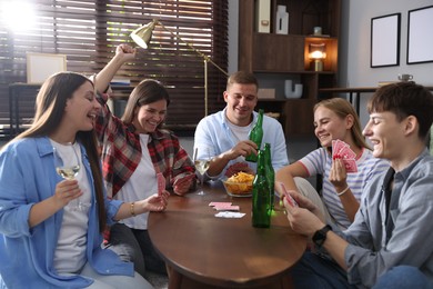 Photo of Group of friends playing cards at wooden table indoors