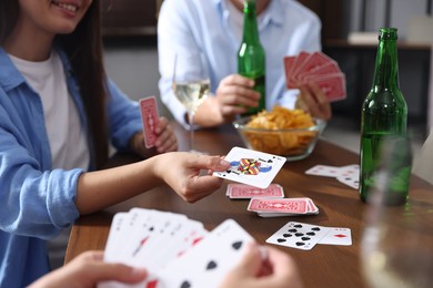 Photo of Friends playing cards at wooden table indoors, closeup