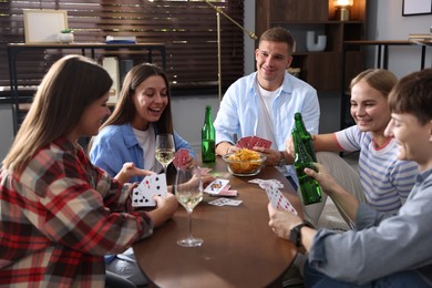 Photo of Group of friends playing cards at wooden table indoors