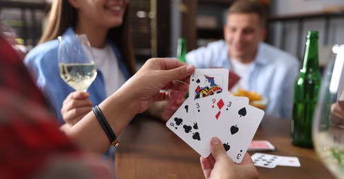 Photo of Friends playing cards at wooden table indoors, selective focus