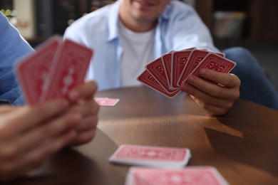 Photo of Friends playing cards at wooden table indoors, selective focus
