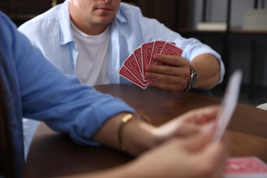 Photo of Friends playing cards at wooden table indoors, closeup