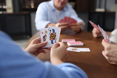Photo of Friends playing cards at wooden table indoors, selective focus