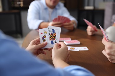 Photo of Friends playing cards at wooden table indoors, selective focus