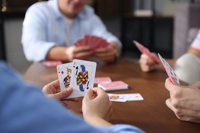 Photo of Friends playing cards at wooden table indoors, selective focus