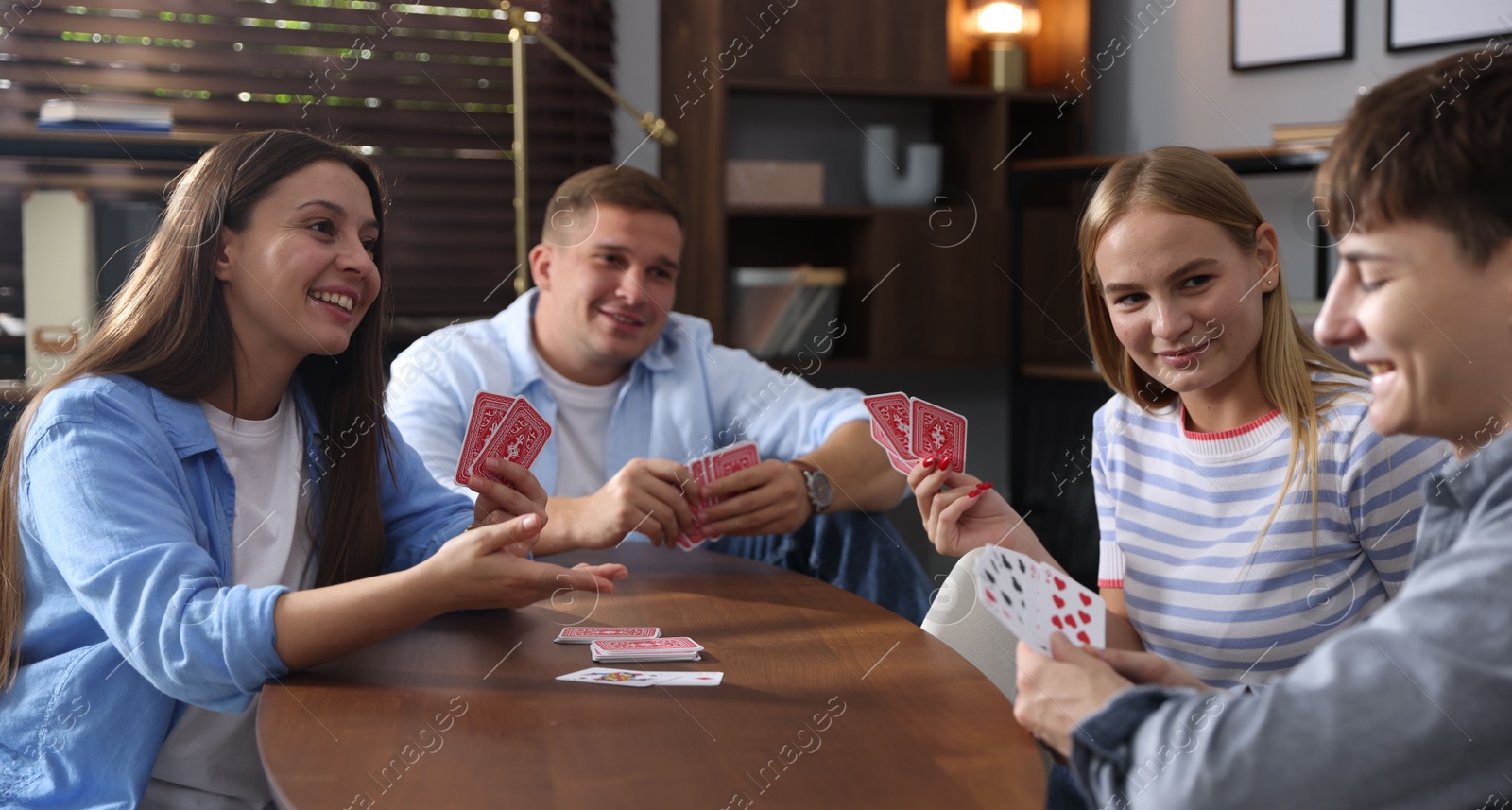 Photo of Group of friends playing cards at wooden table indoors